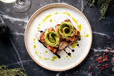 Modern bir tabakta taze sebzeli, otlu ve sanatsal kaplamalı zarif avokado tostu.