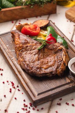 Kızarmış sebze ve ahşap bir tahtanın üstünde barbekü sosuyla servis edilen sulu ızgara biftek.