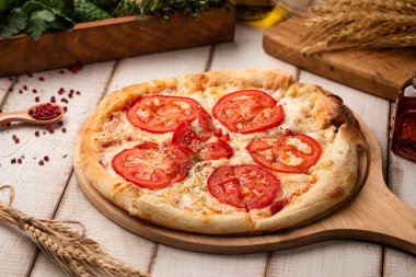 Ev yapımı pizza dilimlenmiş domates peyniri ve sade ahşap tahtada servis edilen otlarla kaplı.