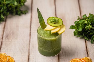 Kivi dilimleri ve kırsal masada nane yapraklarıyla servis edilen sağlıklı taze yeşil smoothie.
