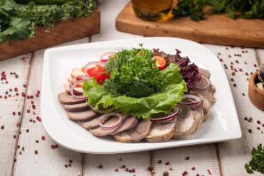 Geleneksel Kazak et tabağında dilimlenmiş kazy zhaya soğanı taze otlar ve marul garnitürü var.