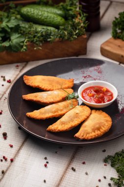 Altın çıtır mini chebureki tabakta ve bol baharatlı domates sosuyla servis ediliyor.