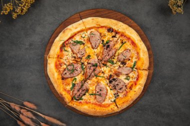 Dilimlenmiş et, peynir ve otlarla kaplı yumuşak ahşap bir tahtanın üzerinde ördek pizzası.