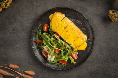 Hardal soslu ızgara tavuk filetosu ve koyu tabakta taze salata.