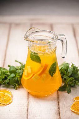 Narenciye limonatasını nane yaprakları ve buzla yenilemek. Tahta masadaki cam sürahide servis edilir.