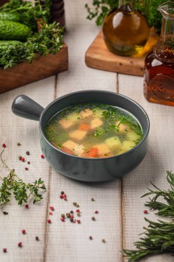 Sıcak somon çorbası, şifalı otlar ve sebzeler kırsal masada, koyu kâsede.