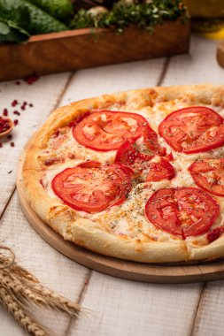 Ev yapımı pizza dilimlenmiş domates peyniri ve sade ahşap tahtada servis edilen otlarla kaplı.