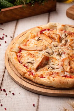 Erimiş peynir ve bitkilerle ahşap tahta üzerinde klasik tavuk mantarlı pizza.