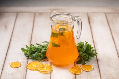 Naneli, portakal dilimli ve kırsal ahşap masada servis edilen cam sürahide servis edilen buzlu narenciye suyu.