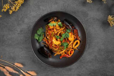 Karides, midye ve sebzeli baharatlı deniz ürünleri makarnası. Bol soslu ve koyu otlu bir tabakta servis ediliyor.