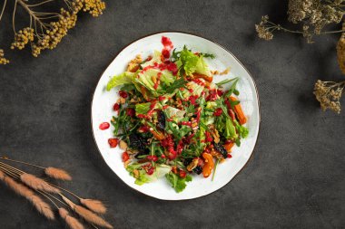 Beyaz tabakta servis edilen taze salata, kızarmış sebze, fındık ve çilek sosu.