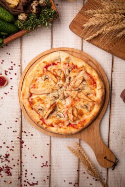 Erimiş peynir ve bitkilerle ahşap tahta üzerinde klasik tavuk mantarlı pizza.