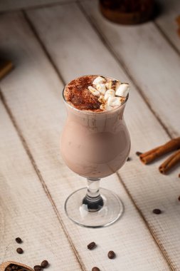 Kakao tozu ve marşmelovla kaplanmış kremalı çikolatalı içecek kırsal ahşap masada servis edilir.