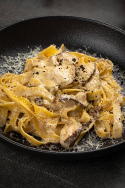 Mantarlı ve peynirli kremalı tagliatelle makarnası siyah bir tabakta servis ediliyor.