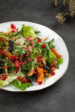 Beyaz tabakta servis edilen taze salata, kızarmış sebze, fındık ve çilek sosu.