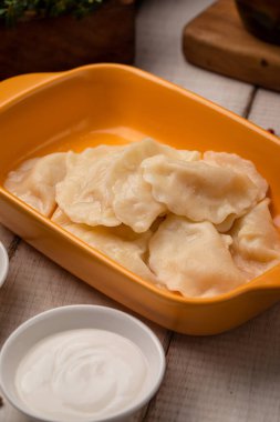 Kaynamış vareniki köfteleri taze otlar ve kaymak gibi ahşap arka planda kremalı sosla servis edilir.