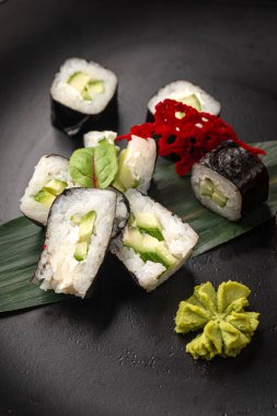 Zencefilli wasabi ve soya soslu siyah tabakta servis edilen salatalıklı vejetaryen suşi ruloları.