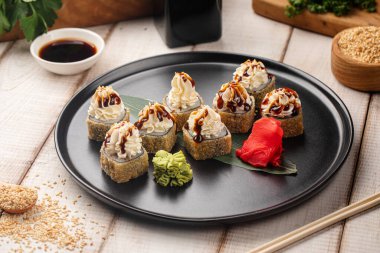 Zencefil ve wasabi ile servis edilen kremalı sosla kaplı çıtır tempura suşi ruloları.