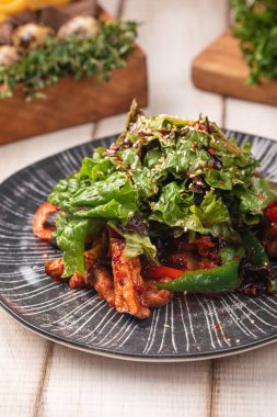 Baharatlı tavuk salatası, kızarmış yeşillikler, taze domatesler ve koyu bir tabakta servis edilen lezzetli soslar.