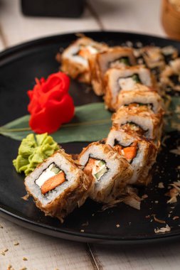 Zencefil ve wasabi ile servis edilen siyah tabakta kurutulmuş ton balığı ile kaplı bonito suşi ruloları.