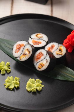 Yin yang suşisi, wasabi ve zencefilli siyah bir tabakta servis edilen yılan balığı ve somon balıklı rulo.