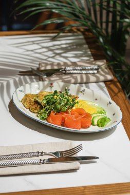 Füme somon dilimleri taze yeşillik kabaklı börek ve limonla servis edilir. Zarif bir restoran ortamında beyaz bir tabakta.