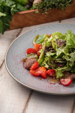 Taze et salatası, yeşil yapraklı, kiraz domatesli ve sade bir masada seramik tabakta servis edilen hafif soslu.
