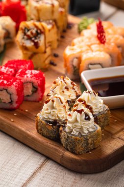 Ahşap bir tahtada soslar ve süslemelerle servis edilen çeşit çeşit suşi ruloları.