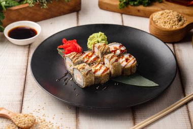 Kızarmış suşi rulo balık krem peynirli ve soslu pilav ve siyah tabakta susamlı.