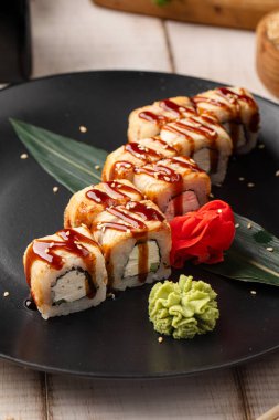 Izgara suşi, pirinç balığı ve krem peynirle birlikte siyah tabakta servis edilen tatlı soslu.