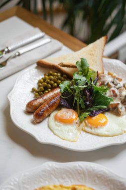 İngiliz usulü kahvaltı, sahanda yumurta sosis, bezelye tostu ve tabakta taze salata.