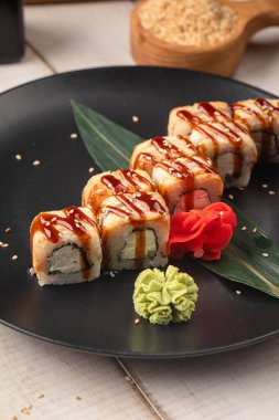 Izgara suşi, pirinç balığı ve krem peynirle birlikte siyah tabakta servis edilen tatlı soslu.