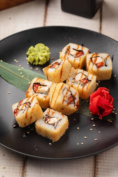 Soslu çıtır tempura suşi ruloları ve zencefil ve wasabi ile servis edilen siyah bir tabakta susam tohumları.
