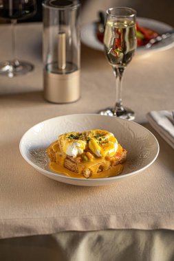 Haşlanmış yumurtalı omlet, kızarmış ekmek ve kremalı hollandez sosu beyaz kasede servis ediliyor.