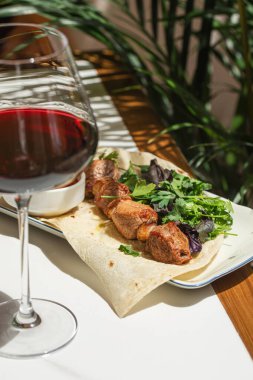 Lezzetli ızgara şiş taze otlu ekmek üzerine servis edilir ve restoran masasında şarap ve anlamlı güneş ışığı gölgeleri ile sos.