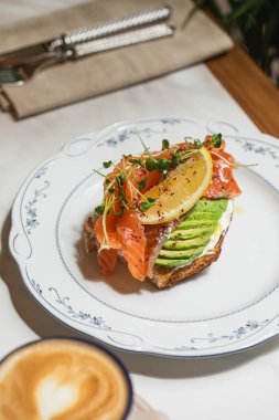 Taze somon dilimleri, mikroçerezler ve beyaz tabakta servis edilen baharatlarla kaplı avokado tostu.