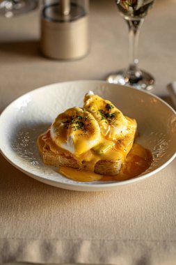 Haşlanmış yumurtalı omlet, kızarmış ekmek ve kremalı hollandez sosu beyaz kasede servis ediliyor.