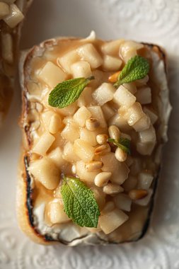 Karamelli armut ve peynirli gurme bruschetta, ılık gölgelerle yumuşak doğal ışıkta fotoğraflanmış.