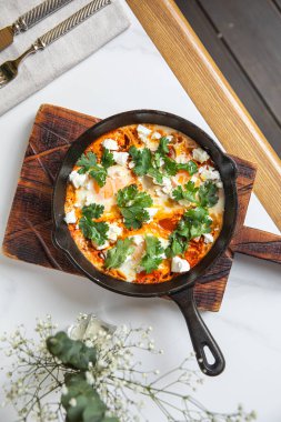 Geleneksel Shakshuka tavada pişirilir. Domatesli. Yumurta, peynir ve kahvaltıda taze otlar.