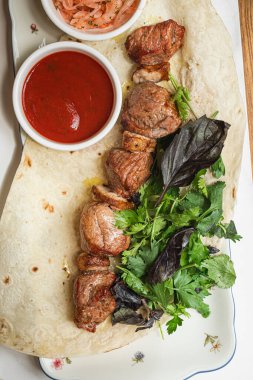 Yumuşak etten yapılmış sulu kuzu şiş taze otlarla servis edilen taze et ve tabakta kırmızı sos.