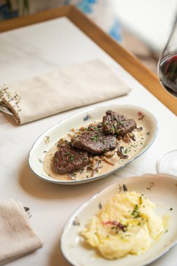 Lokanta masasında nefis tabakta kremalı mantar sosunda servis edilen yumuşak sığır eti madalyonları.