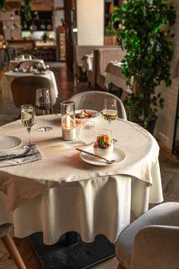 Tatlı şarap kadehleri, mum ve sofra takımı ile güzel bir yemek deneyimi için hazırlanmış rahat bir restoran masası.