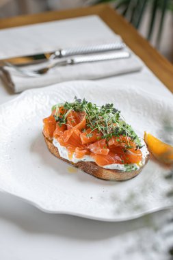 Taze somon dilimleri, mikroçerezler ve beyaz tabakta servis edilen baharatlarla kaplı avokado tostu.
