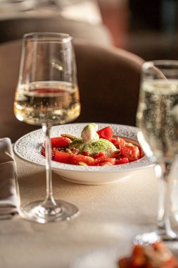 Taze burrata peyniri, olgun domates fesleğen ve zeytin yağı. Restoran masasında beyaz şarapla servis ediliyor.