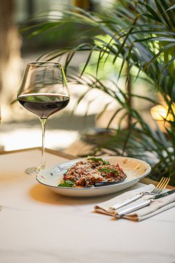 Eritilmiş peynirle kaplı fırında patlıcan yarımları ve restoran ortamında servis edilen taze fesleğen.