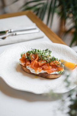 Üstü füme somon krem peynirli mikroçerez ve narenciye ile kaplı. Zarif beyaz tabakta servis ediliyor.