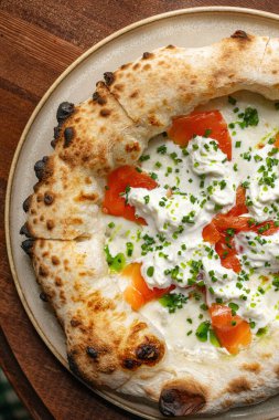 İtalyan usulü üzerine füme somon peyniri ve ahşap masada servis edilen taze soğanlı pizza.