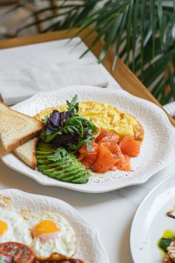 Çırpılmış yumurtalı restoran kahvaltısı somon balığı taze yeşillikler ve beyaz tabakta kızarmış ekmek.