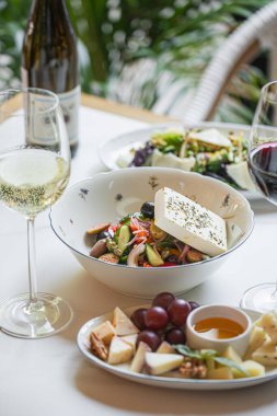 Peynirli sebze, zeytin ve beyaz şarap ve peynir tabağıyla servis edilen bitkilerle taze restoran salatası.