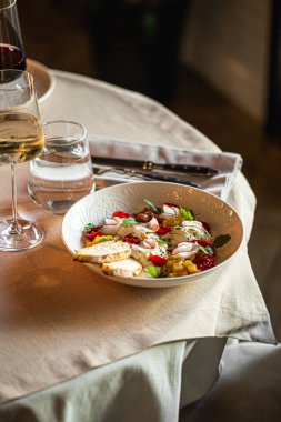 Stracciatella peynirli salata ve çeşitli domatesler şık bir restoran masasında servis edilir.